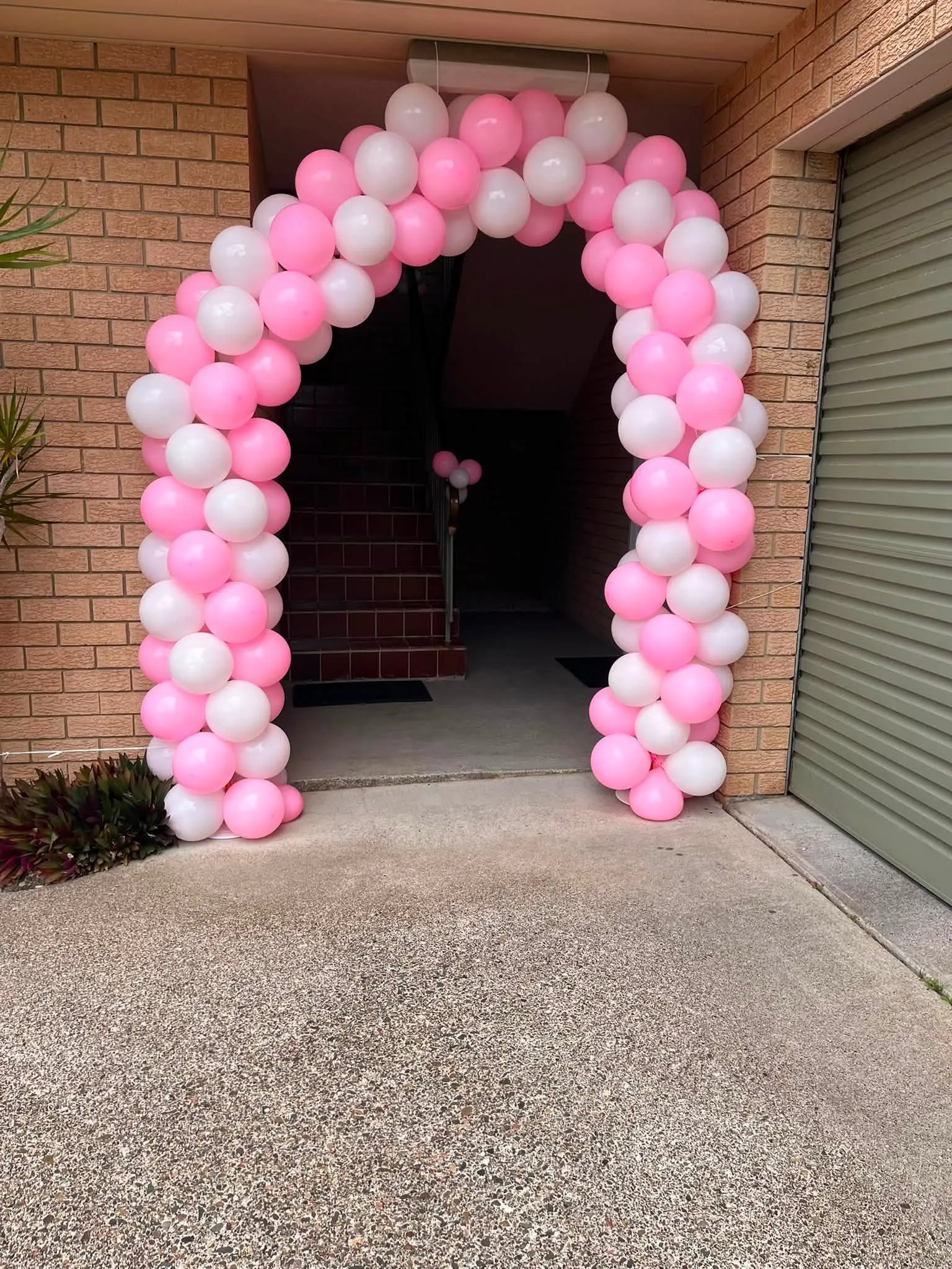 Pink and white balloon arch framing a doorway for a birthday party