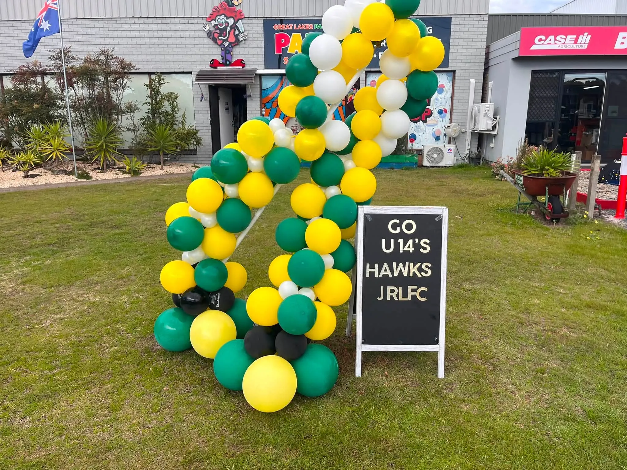 Green and gold club-colour balloon garland set up on the lawn outside the store