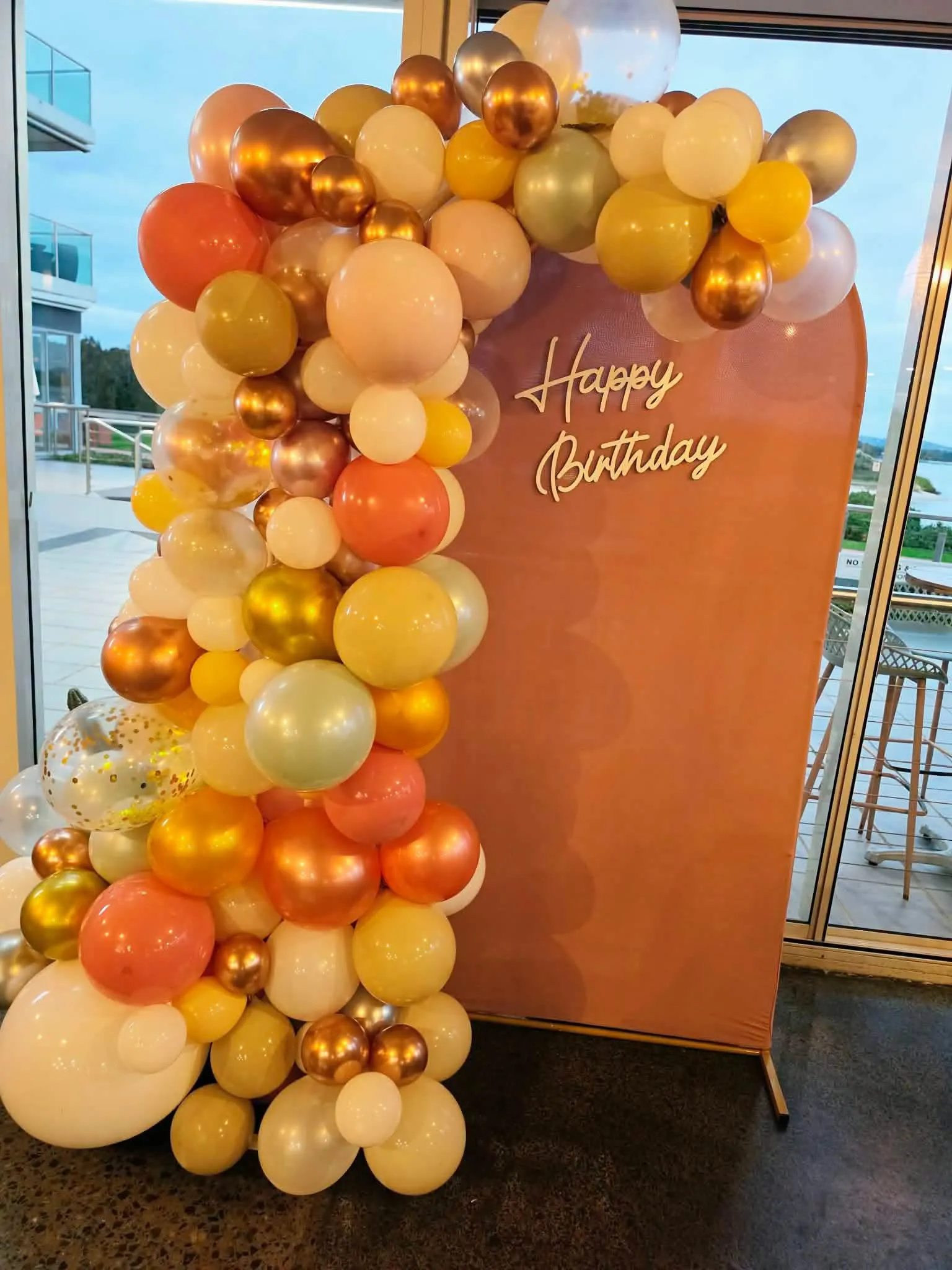 Gold, copper and cream balloon garland arcing over a Happy Birthday backdrop board