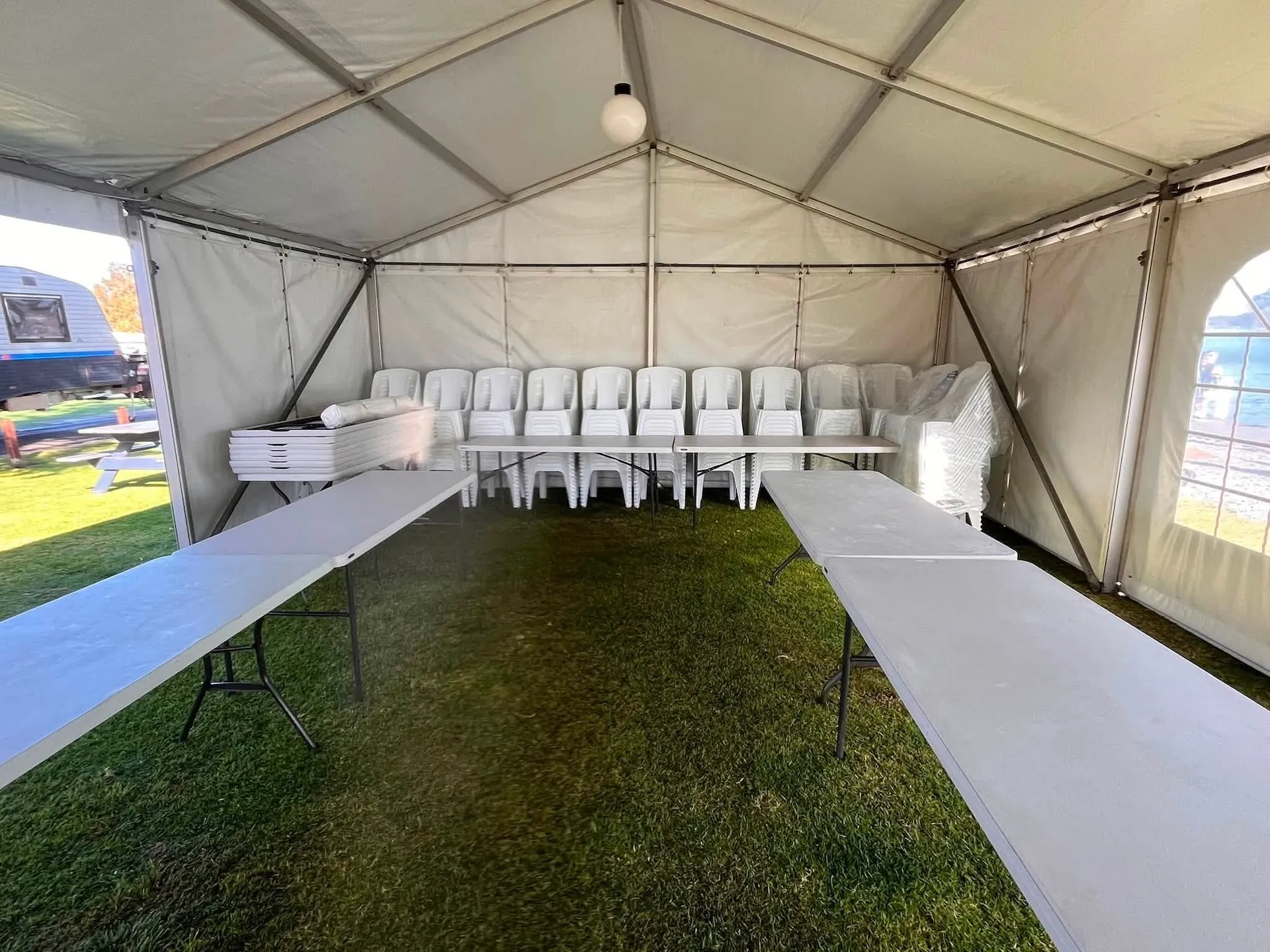 Trestle tables and stacked white chairs part-way through a function setup