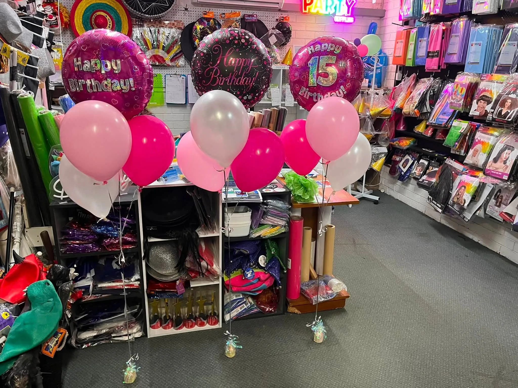 Birthday balloon bouquets on display in front of shelves of party goods in store