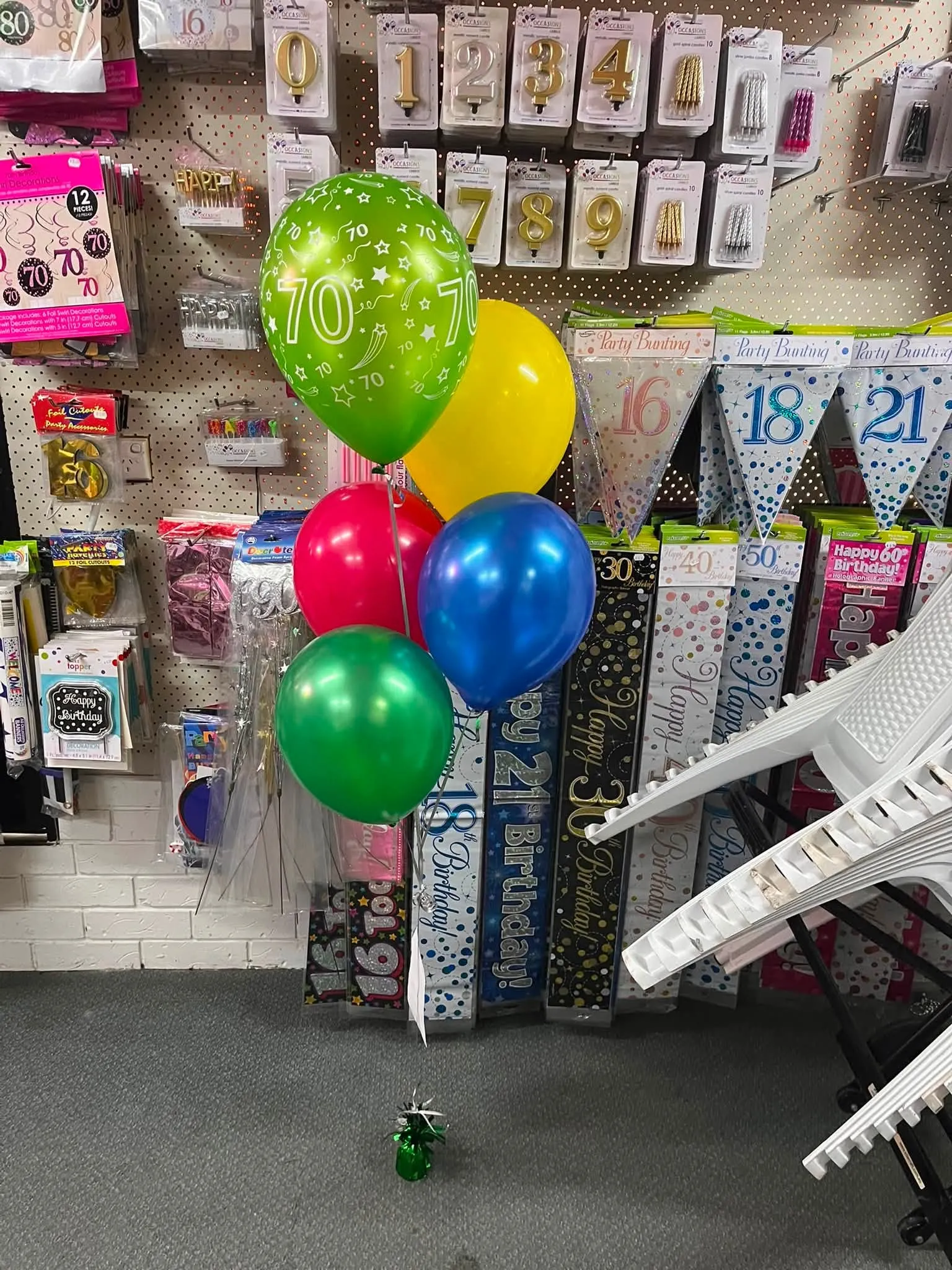 Helium balloon bunch in green, red, yellow and blue made up in store beside milestone birthday balloons