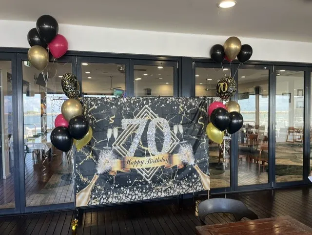 70th birthday party setup with black and gold balloons and a sequin backdrop
