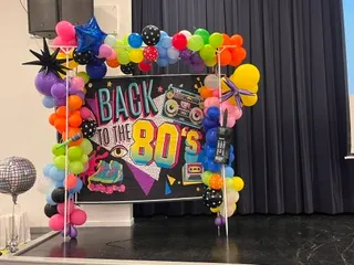 Back to the 80s themed party backdrop with a rainbow balloon garland